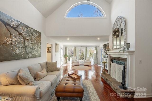 living room featuring recessed lighting, high vaulted ceiling, a fireplace with raised hearth, and wood finished floors