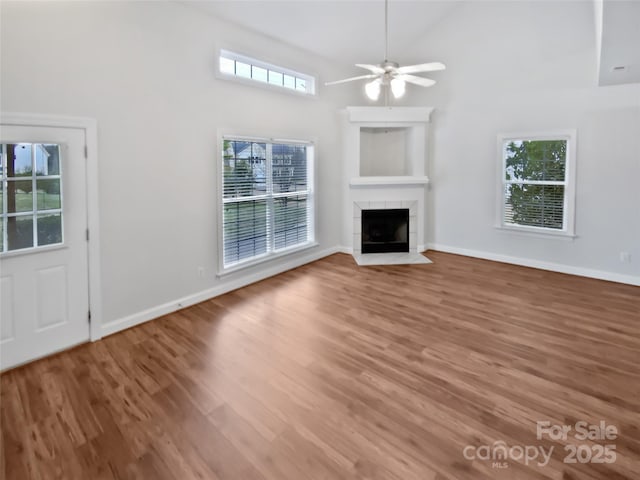 unfurnished living room featuring a wealth of natural light, a tile fireplace, high vaulted ceiling, and wood finished floors