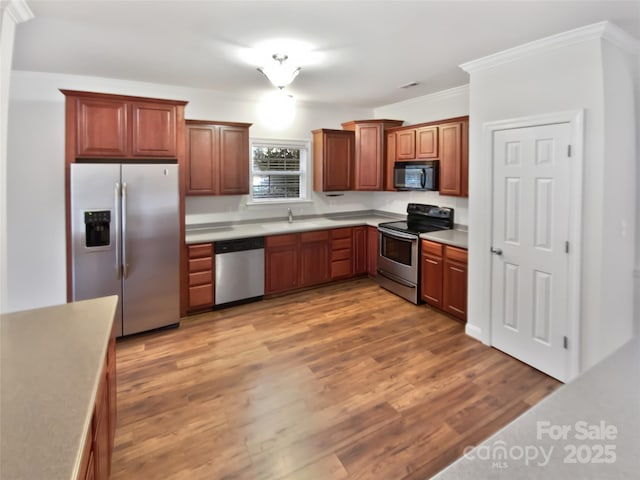 kitchen featuring stainless steel appliances, light countertops, light wood-style floors, ornamental molding, and a sink