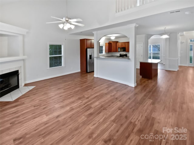 unfurnished living room with a towering ceiling, arched walkways, a ceiling fan, and a tile fireplace