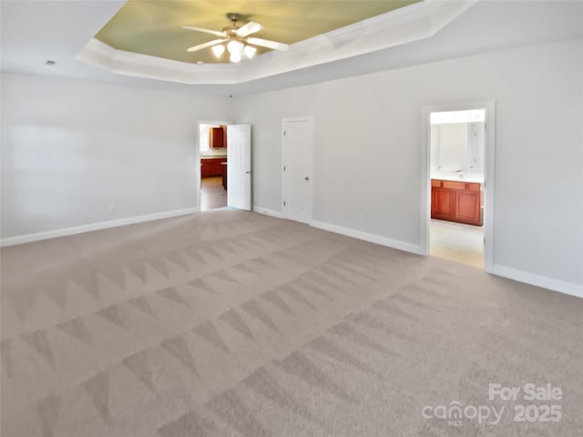 empty room with a raised ceiling, light carpet, ceiling fan, and baseboards