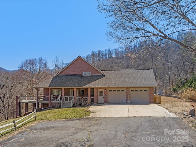 view of front of house with a porch, concrete driveway, a wooded view, a garage, and brick siding