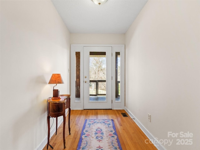 doorway to outside featuring baseboards, visible vents, and light wood finished floors