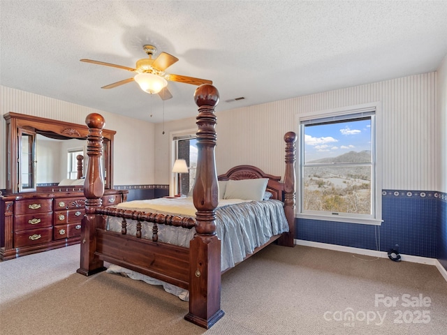 carpeted bedroom with visible vents, a textured ceiling, a ceiling fan, and wallpapered walls