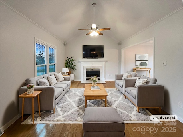 living area with vaulted ceiling, a fireplace with flush hearth, ornamental molding, and wood finished floors