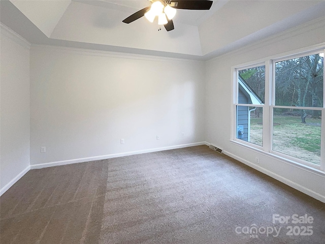 empty room with dark carpet, a raised ceiling, visible vents, and baseboards