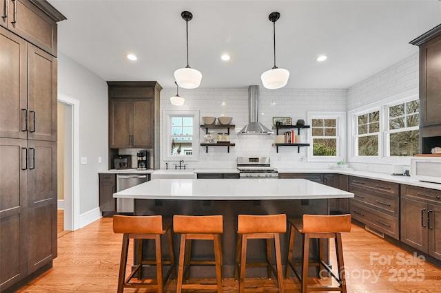 kitchen featuring decorative backsplash, wall chimney exhaust hood, appliances with stainless steel finishes, light countertops, and open shelves