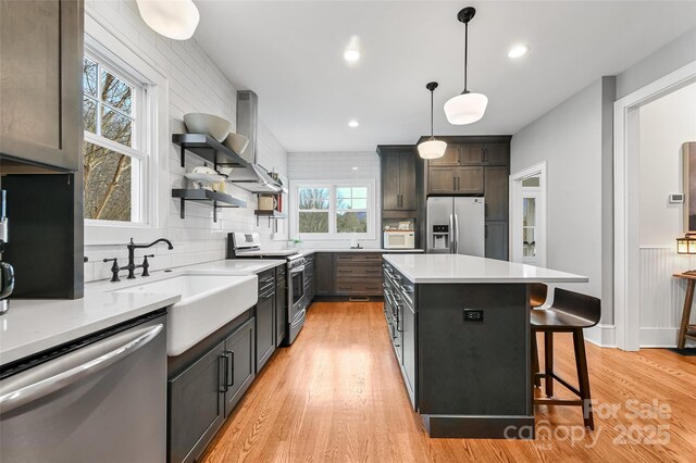 kitchen with a breakfast bar area, stainless steel appliances, light wood-type flooring, open shelves, and a sink