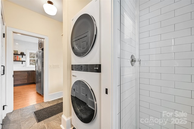 washroom featuring baseboards, laundry area, light wood-style flooring, and stacked washer / drying machine