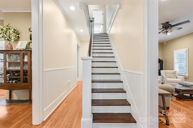 stairway featuring wainscoting, wood finished floors, a ceiling fan, and crown molding