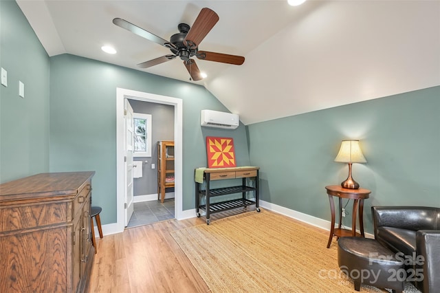 sitting room with ceiling fan, wood finished floors, baseboards, vaulted ceiling, and a wall mounted air conditioner