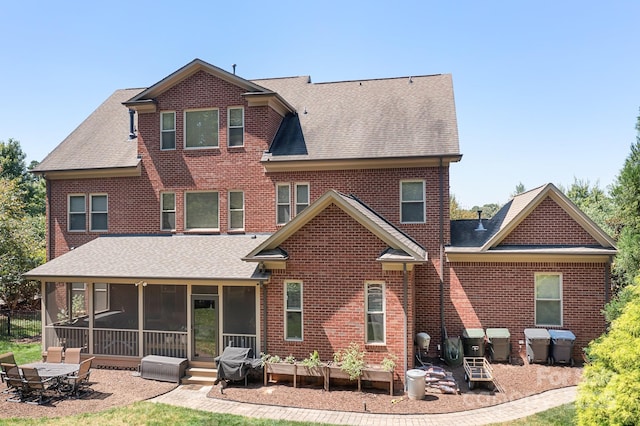 back of house featuring brick siding, a sunroom, and a shingled roof