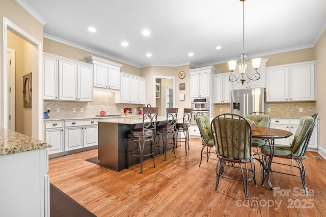 kitchen with light wood-type flooring, a kitchen island with sink, white cabinets, a kitchen bar, and stainless steel fridge