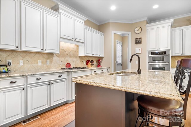 kitchen featuring a sink, a kitchen breakfast bar, white cabinetry, stainless steel appliances, and crown molding