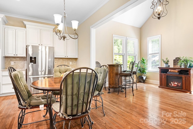 dining room featuring a chandelier, light wood finished floors, a warm lit fireplace, and ornamental molding