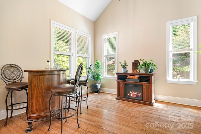 bar featuring a glass covered fireplace, baseboards, light wood-type flooring, and lofted ceiling