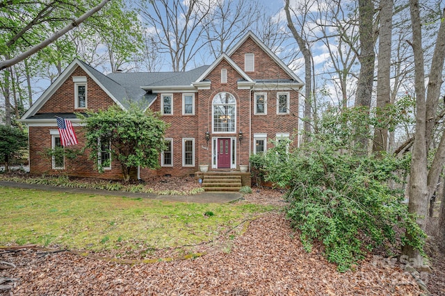 view of front facade featuring brick siding, a front yard, and a shingled roof