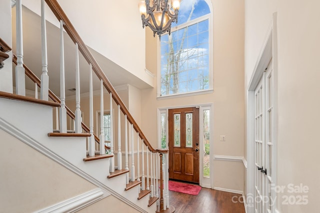 entryway with wood finished floors, a towering ceiling, stairway, and an inviting chandelier