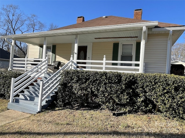 bungalow featuring covered porch, roof with shingles, and a chimney