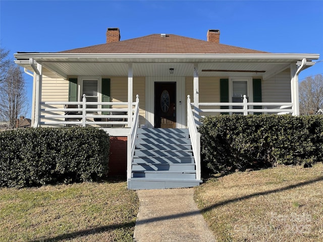 bungalow with a porch, a shingled roof, and a chimney