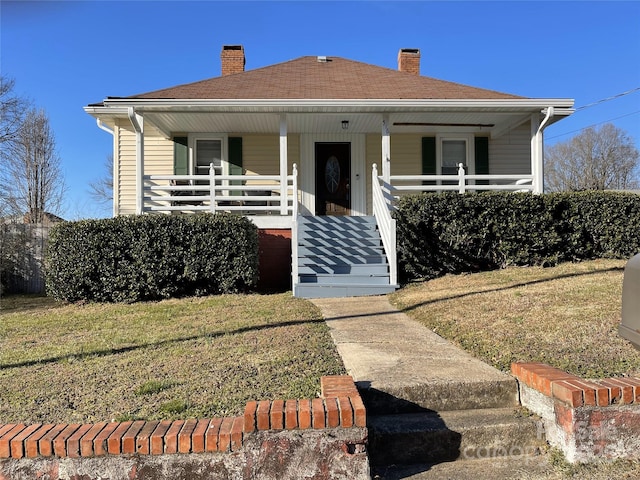 bungalow featuring a front yard, covered porch, and a chimney