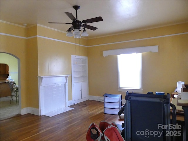 office area with arched walkways, ornamental molding, ceiling fan, wood finished floors, and baseboards