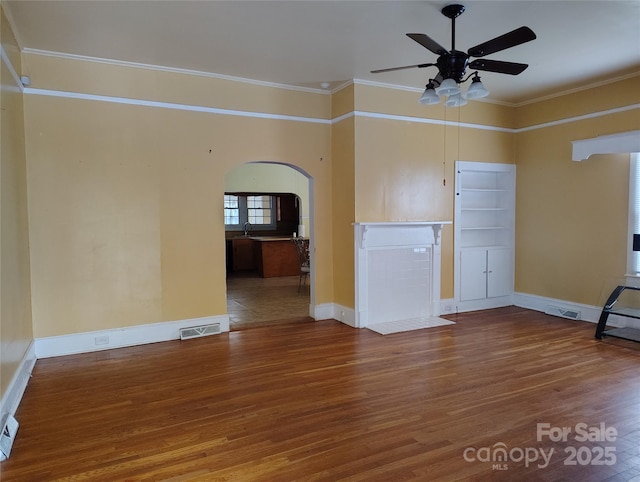 unfurnished living room featuring wood finished floors, a ceiling fan, visible vents, arched walkways, and ornamental molding