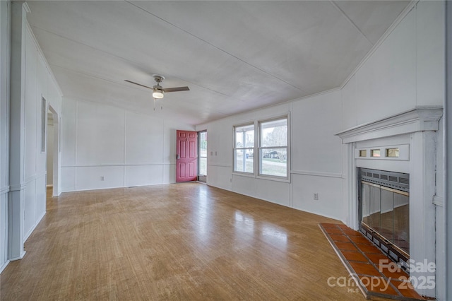 unfurnished living room featuring ceiling fan, a glass covered fireplace, a decorative wall, and wood finished floors