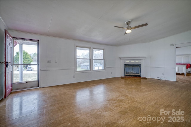 unfurnished living room with a glass covered fireplace, a decorative wall, and ceiling fan