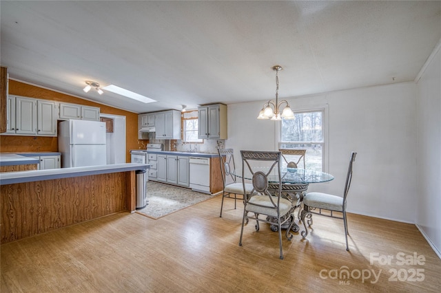 kitchen with a notable chandelier, lofted ceiling, decorative backsplash, light wood-type flooring, and white appliances