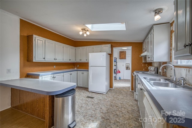 kitchen with white appliances, a skylight, a peninsula, under cabinet range hood, and a sink