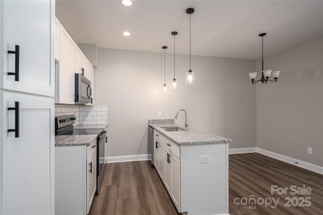 kitchen featuring a peninsula, dark wood-type flooring, a sink, appliances with stainless steel finishes, and backsplash