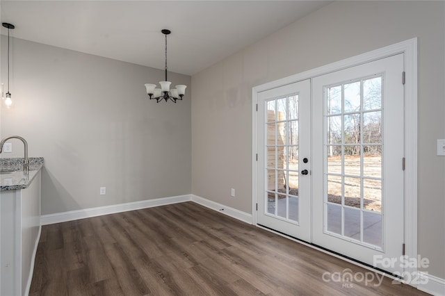 unfurnished dining area featuring baseboards, dark wood-style floors, an inviting chandelier, french doors, and a sink