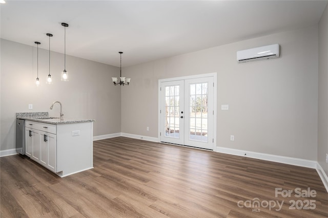 kitchen with a wall unit AC, dark wood-style flooring, light stone countertops, white cabinetry, and a sink