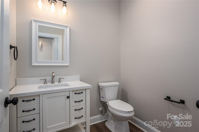 half bathroom with baseboards, vanity, toilet, and wood finished floors