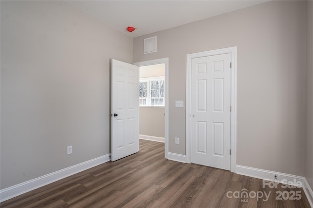 unfurnished bedroom with dark wood-style flooring, visible vents, and baseboards