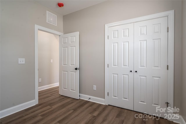 unfurnished bedroom featuring a closet, visible vents, dark wood finished floors, and baseboards