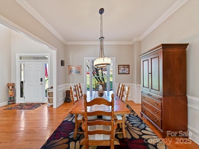 dining space with light wood-style floors, ornamental molding, a decorative wall, and a wainscoted wall