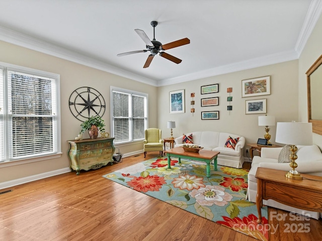 living area with wood finished floors, visible vents, a ceiling fan, baseboards, and ornamental molding