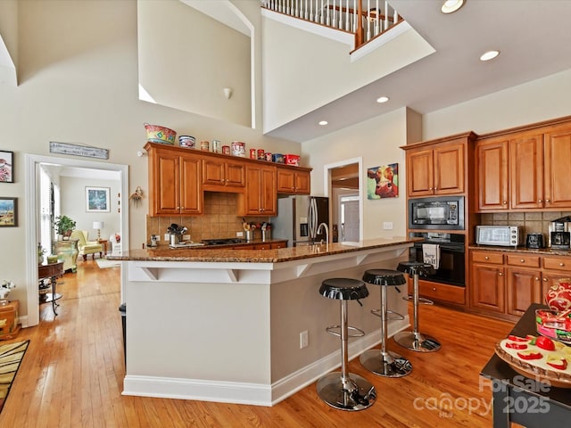 kitchen with brown cabinets, dark stone countertops, light wood-type flooring, black appliances, and a kitchen bar