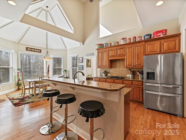 kitchen featuring brown cabinets, light wood finished floors, dark stone counters, stainless steel fridge, and a kitchen breakfast bar