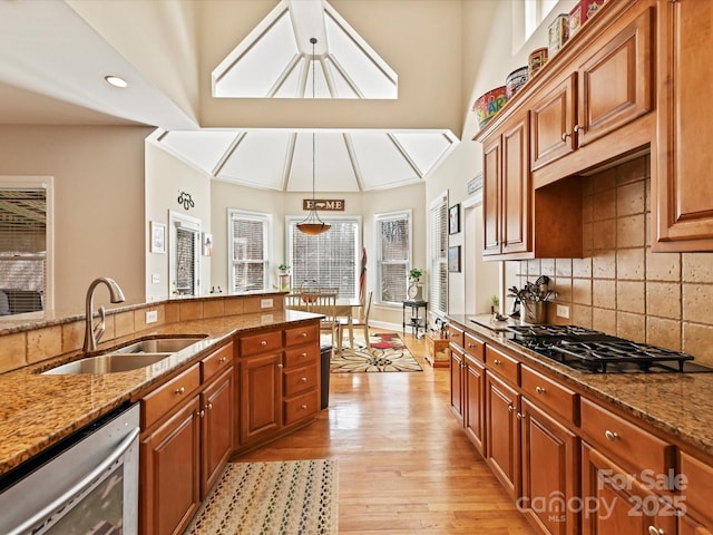 kitchen featuring dishwashing machine, light stone counters, a sink, light wood-style floors, and tasteful backsplash