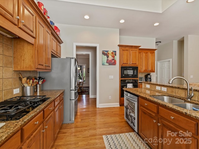 kitchen featuring light wood-type flooring, black appliances, brown cabinets, and a sink