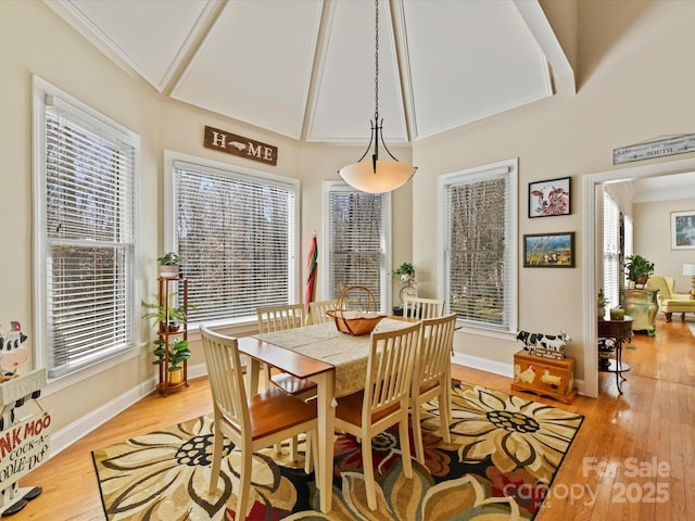 dining room featuring light wood-style floors, a high ceiling, crown molding, and baseboards