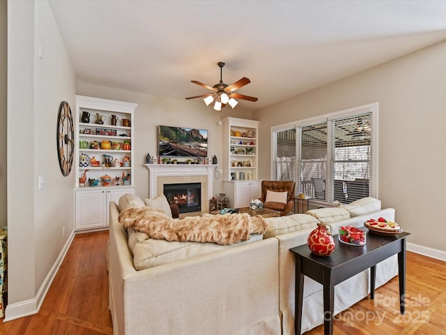 living room featuring a glass covered fireplace, wood finished floors, a ceiling fan, and baseboards