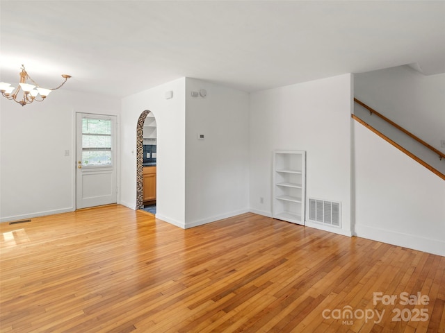 unfurnished room with an inviting chandelier, light wood-style flooring, stairs, and visible vents