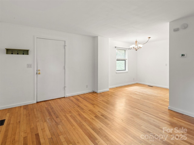 spare room with visible vents, baseboards, light wood-style flooring, and a notable chandelier