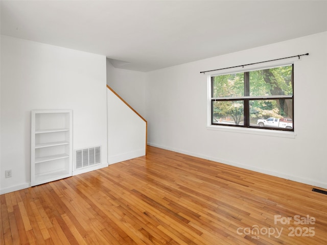 unfurnished room featuring built in features, light wood-type flooring, visible vents, and baseboards