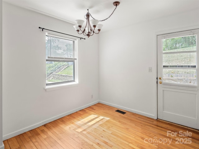 unfurnished dining area with baseboards, visible vents, hardwood / wood-style flooring, and a notable chandelier