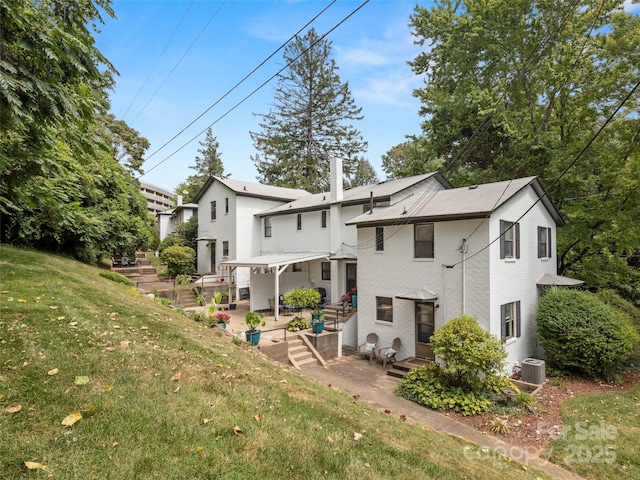 back of property with entry steps, a patio, central AC unit, brick siding, and a lawn